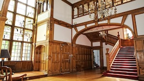 A grand interior with a wooden staircase, large windows, and a chandelier.