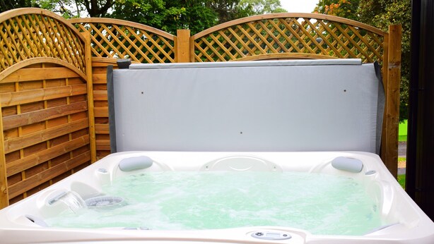 A hot tub with a wooden fence and a metal gate in the background.