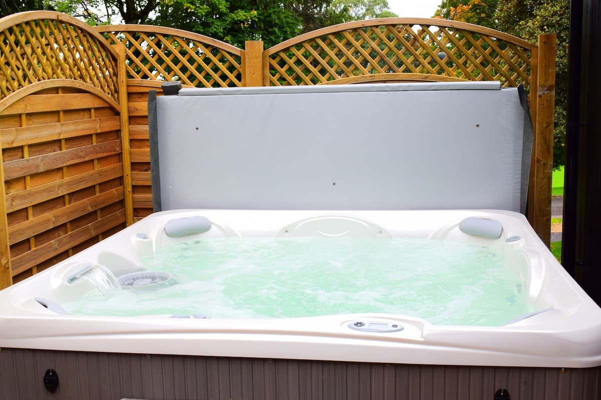 A hot tub with a wooden fence and a metal gate in the background.