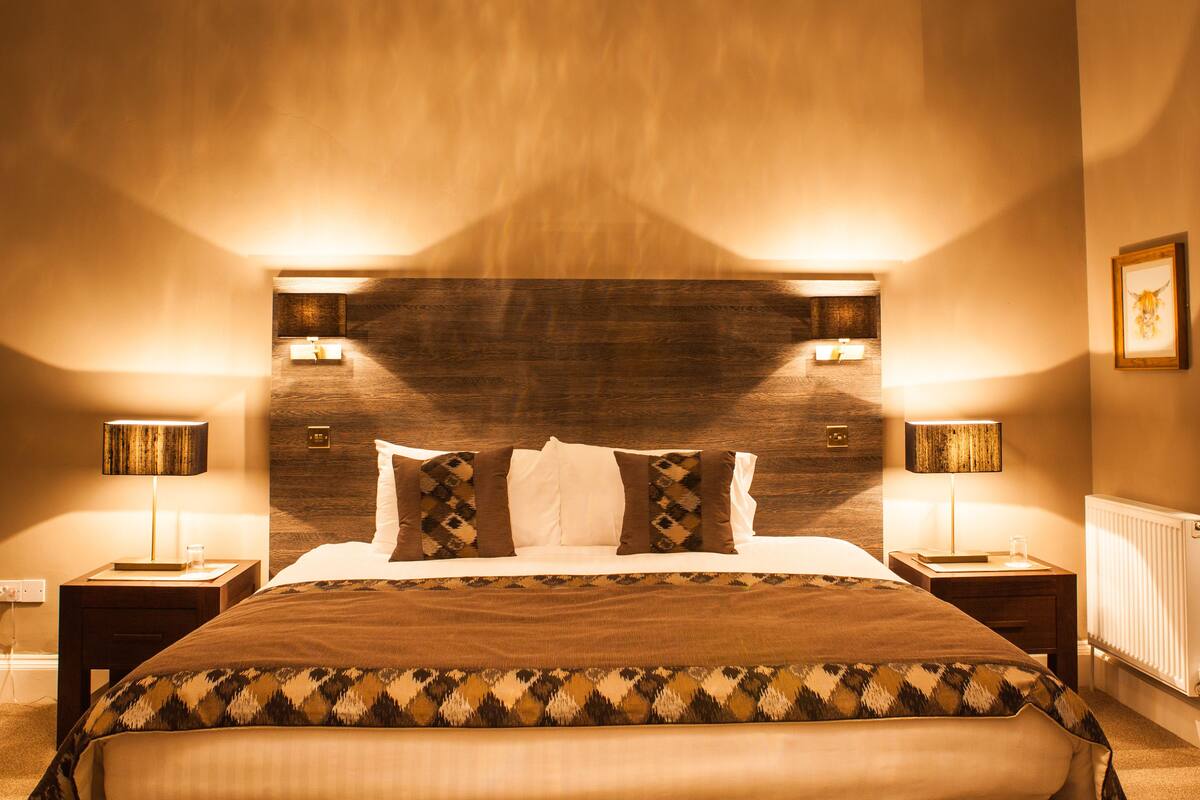 A hotel room with a large bed, two bedside tables with lamps, a wooden headboard, and a framed picture on the wall.