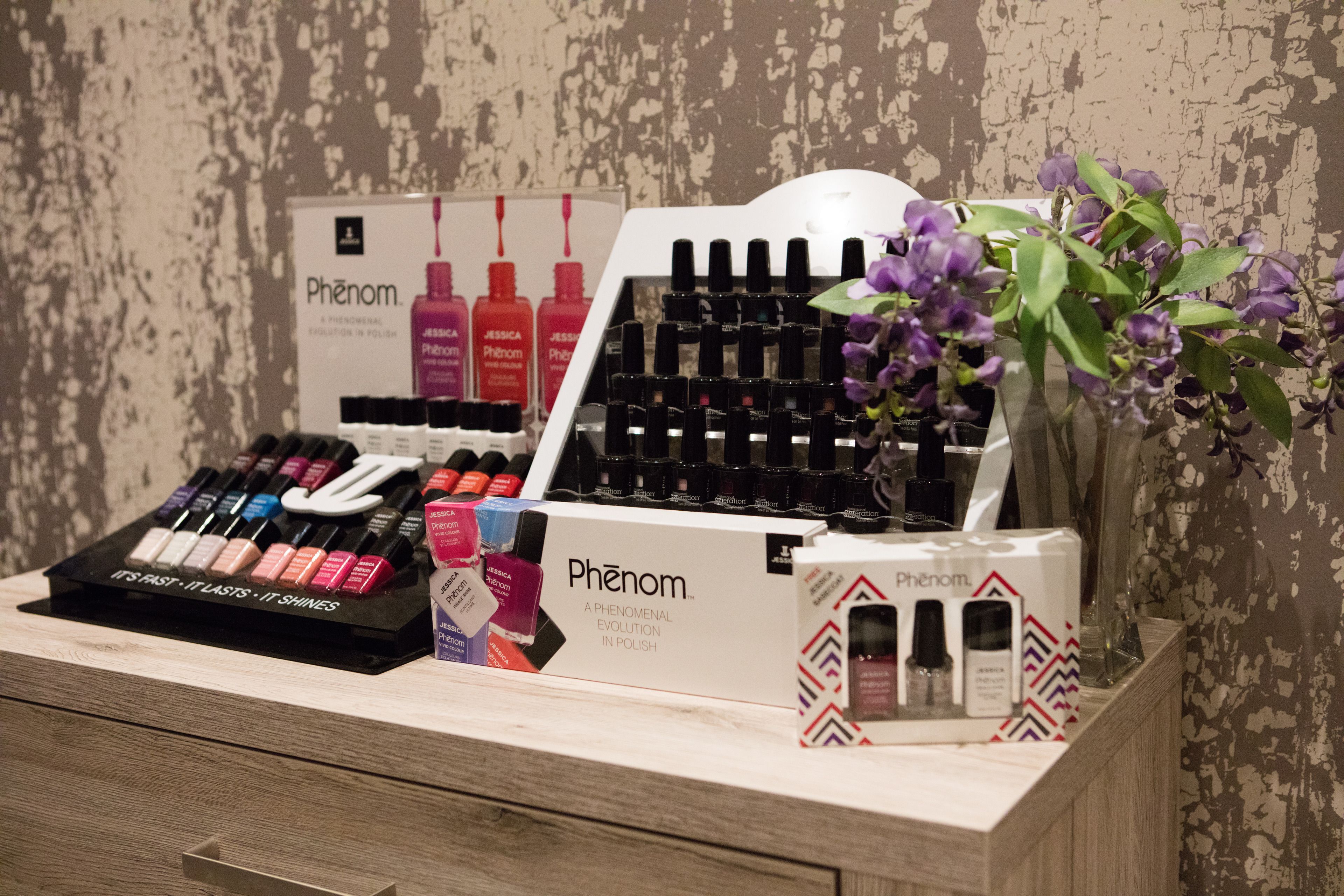 Eine Präsentation von Phénom Nagellackflaschen und -kartons auf einer Holztischplatte mit einer Blumenanordnung.