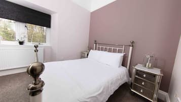A bedroom with a bed, a nightstand, a radiator, and a window with a view of trees.