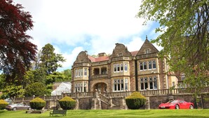 A large, historic building with a prominent entrance, a well-maintained lawn, and a red sports car parked in front.