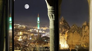 Une vue nocturne depuis un balcon, avec la lune et le paysage urbain en arrière-plan, comprenant une mosquée et des montagnes.