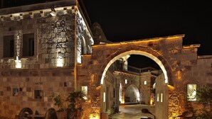 Un bâtiment historique illuminé, doté d’une grande entrée en arc de cercle, de murs en pierre et d’un balcon donnant sur une cour intérieure.
