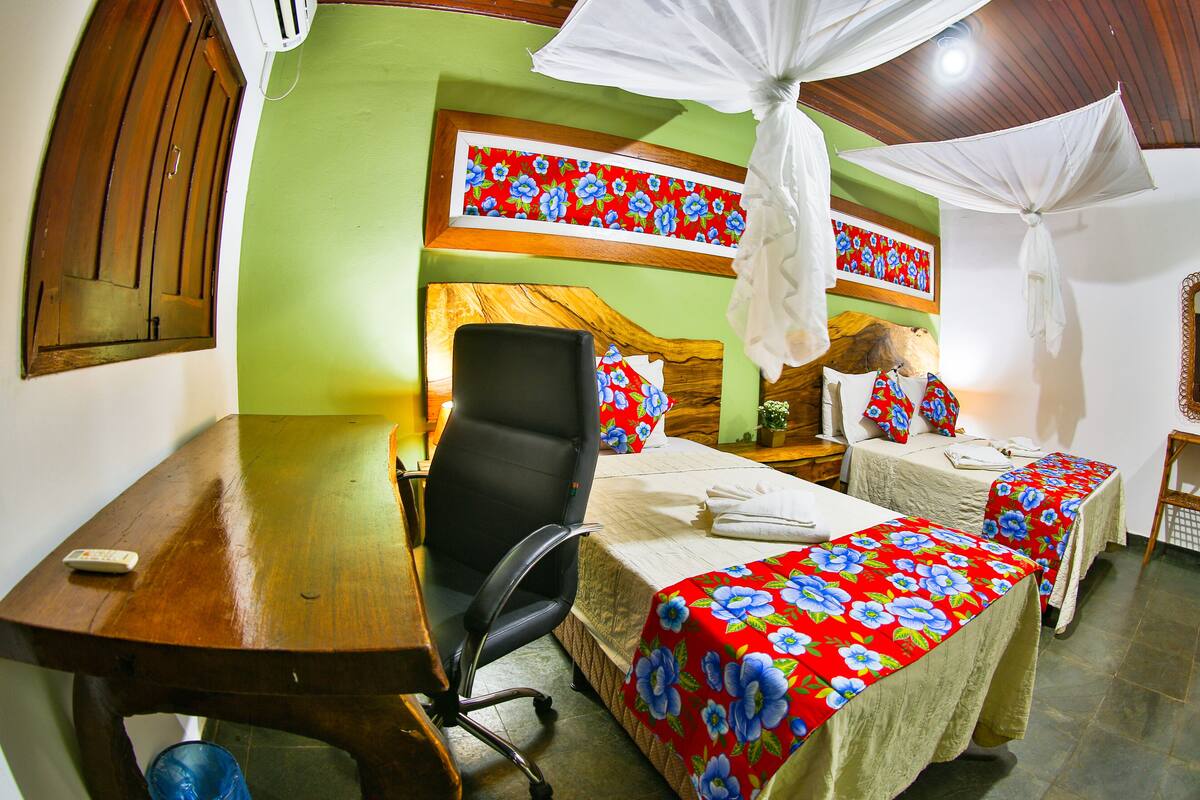 A hotel room with a wooden desk, a black office chair, two beds with floral bedspreads, a wooden headboard, and a mirror on the wall.
