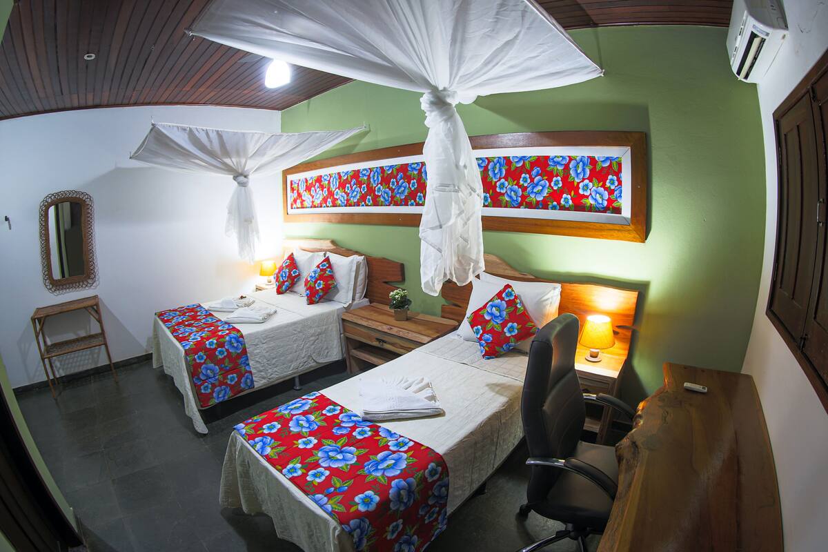 A room with two beds, a desk, a chair, a mirror, and a wall-mounted air conditioner.