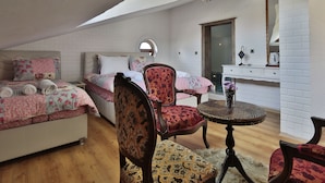 A cozy bedroom with a loft-style ceiling, a bed with floral bedding, two upholstered chairs, a small round table with a vase of flowers, and a white dresser with a mirror. - Cozy Villa Cappadocia (Nevsehir)