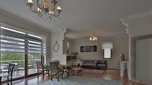 A spacious living room with a large window, a chandelier, and a dining area with wooden furniture. - Cozy Villa Cappadocia (Nevsehir)