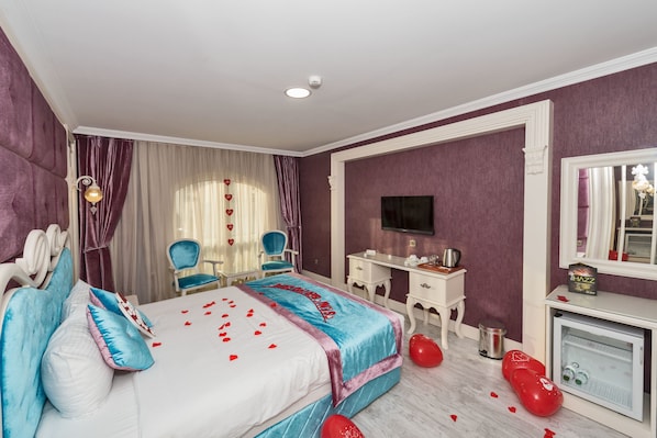A hotel room with a bed, a desk, a chair, a television, and a minibar.