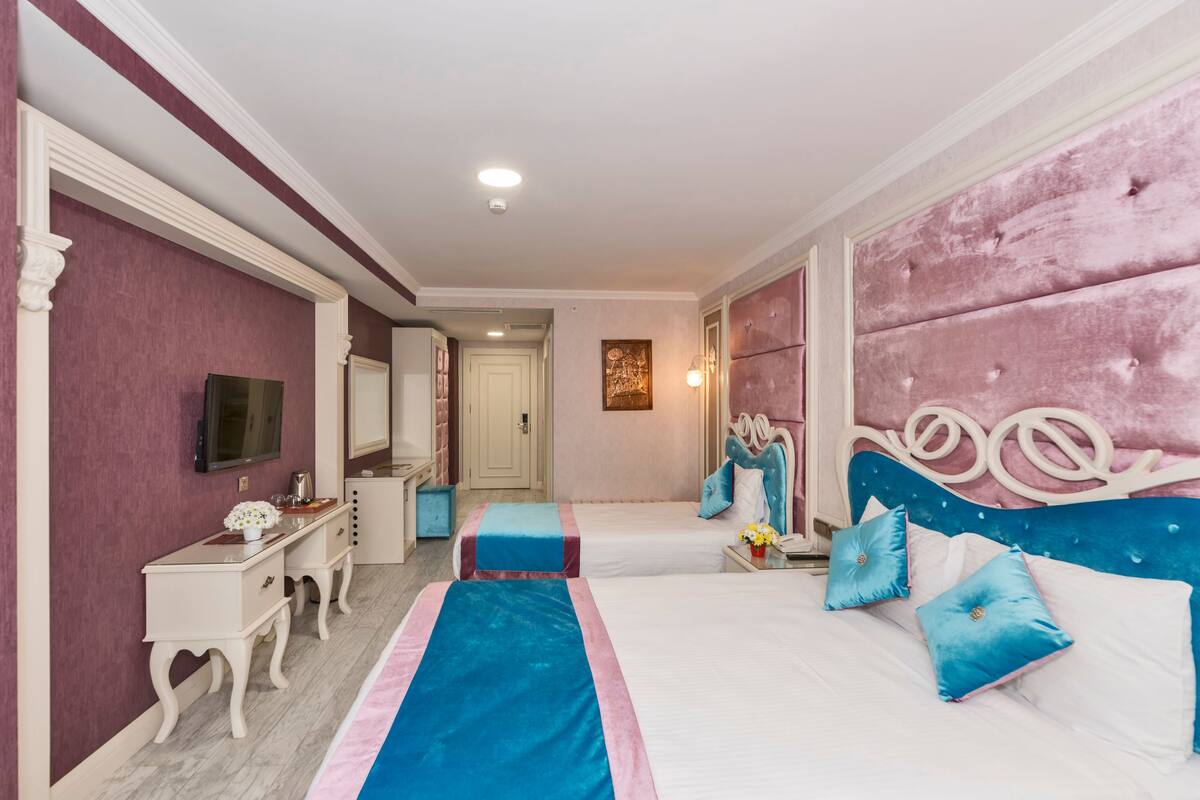 A bedroom with two beds, a vanity with a mirror, and a television on the wall.