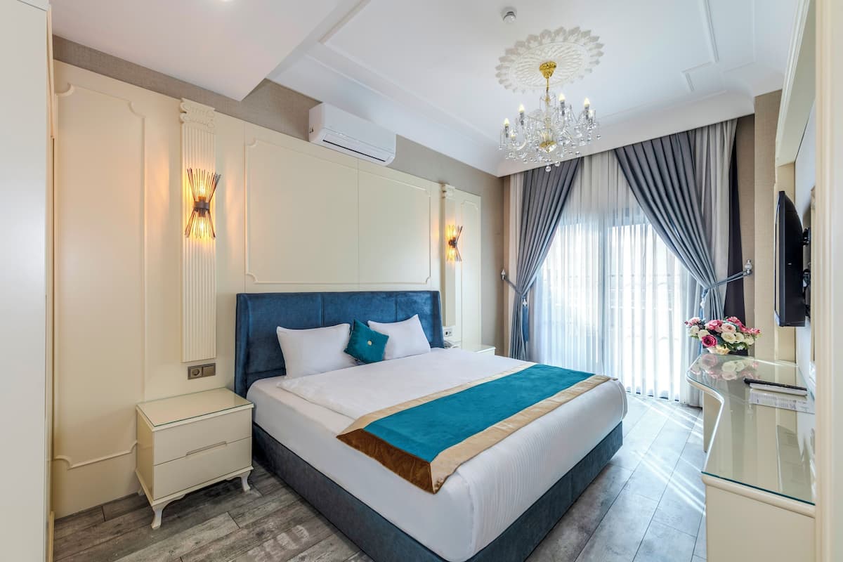 A hotel room with a large bed, bedside tables, a TV, and a chandelier.