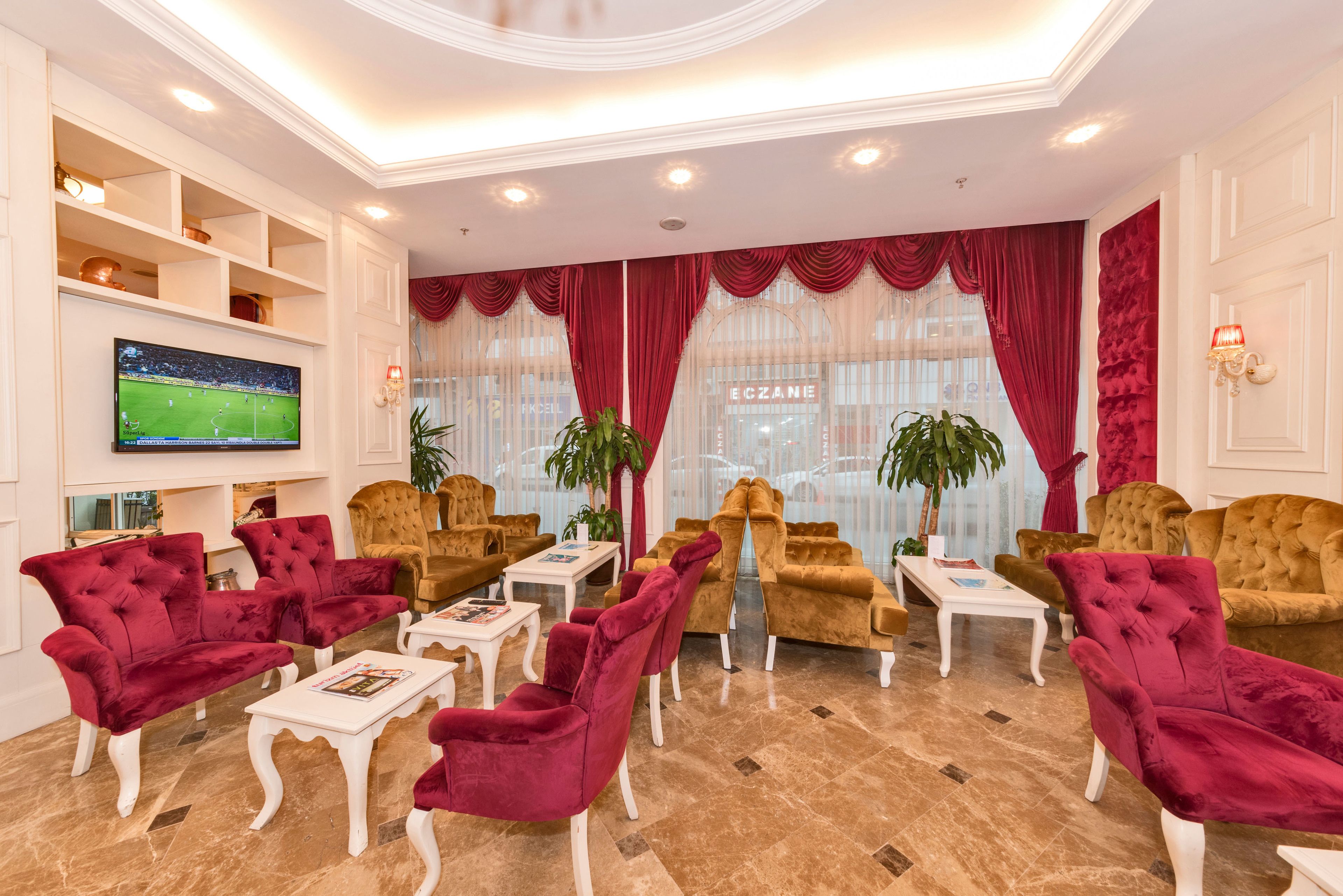 A spacious living room with plush red and gold sofas, a flat-screen TV, and a large window with curtains.