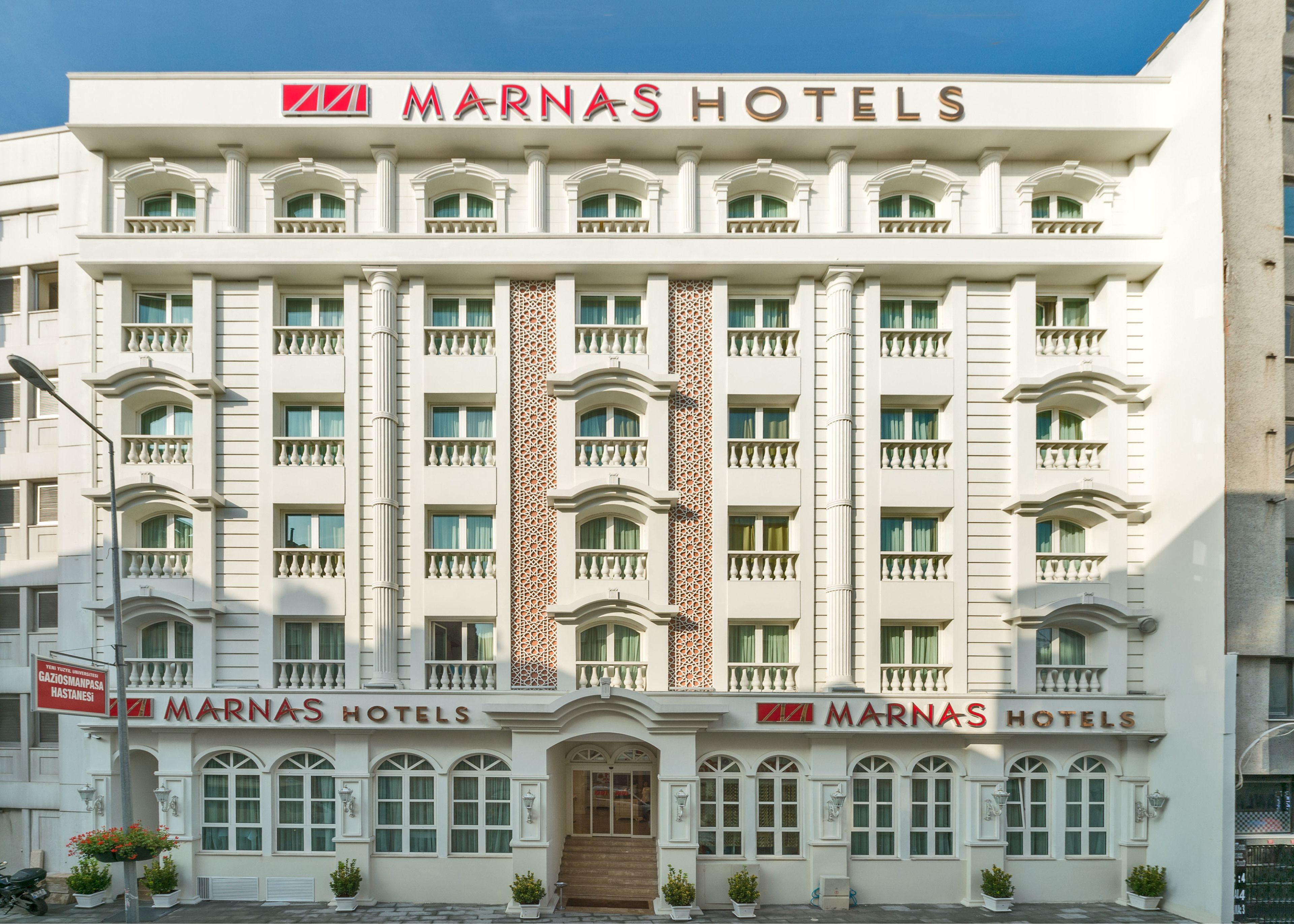 Edifício de vários andares do MARNAS HOTELS, com uma coluna decorativa central, varandas e uma entrada imponente.