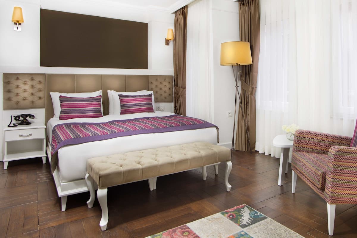 A hotel room with a large bed, a bedside table with a lamp, a chair, and a small table with a vase of flowers.