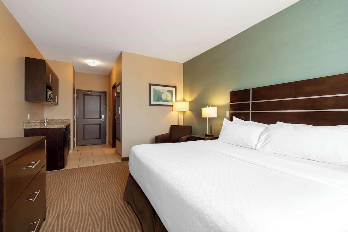 Una habitación de hotel con una cama grande, un escritorio con lavamanos, una silla, una lámpara y una puerta.