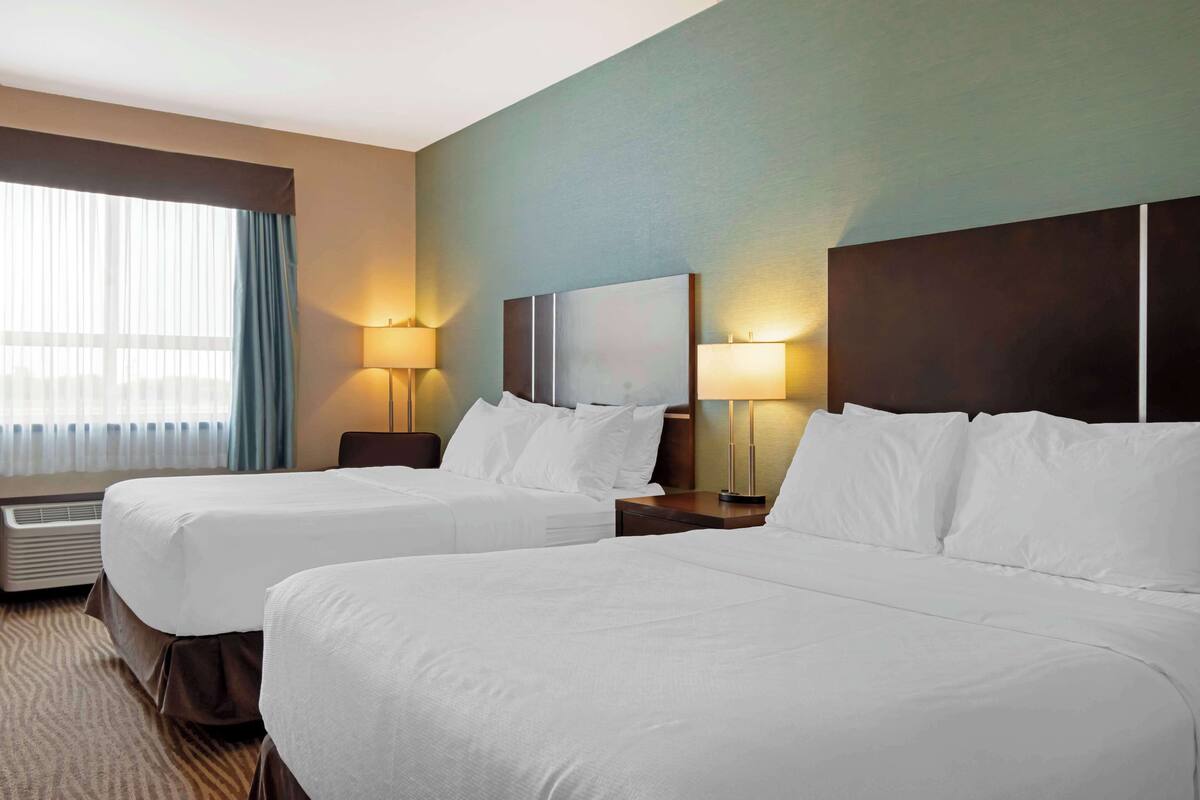 Habitación de hotel con dos camas, un ventanal con cortinas y dos lámparas de noche.