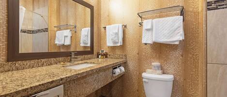 A bathroom with a granite countertop sink, a mirror, a toilet, and a towel rack.