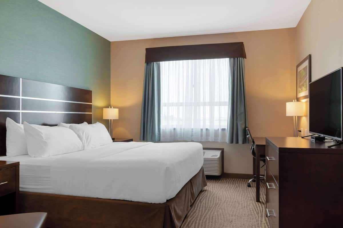 Habitación de hotel con una cama grande, un escritorio con televisor, una lámpara y una ventana con cortinas.
