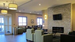 A spacious lobby with a stone wall, a flat-screen TV mounted above a fireplace, and several seating areas with chairs and tables. - Best Western Plus Moosomin Hotel (Moosomin)