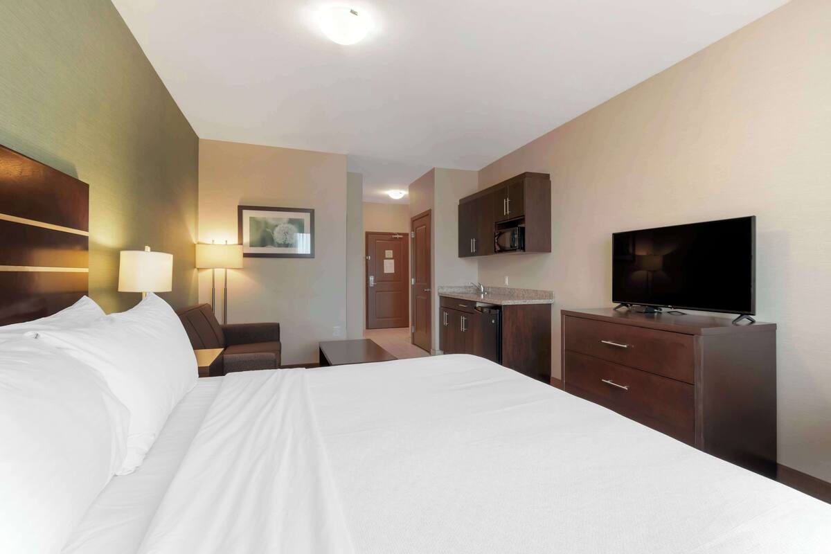Una habitación de hotel con una cama grande, un escritorio, televisión y kitchenette.