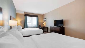 A hotel room with two beds, a desk, a television, and a window with curtains.