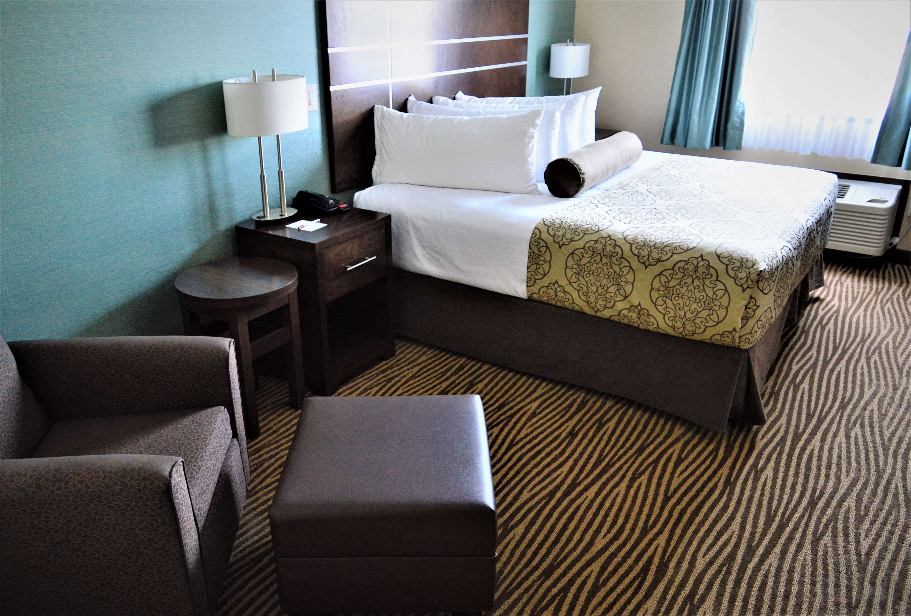 A hotel room with a bed, bedside tables, a lamp, a chair, and a carpeted floor.