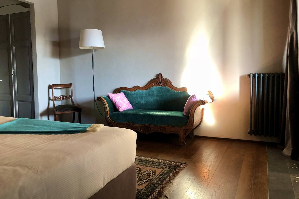 A room with a bed, a green sofa, a chair, a lamp, and a radiator.