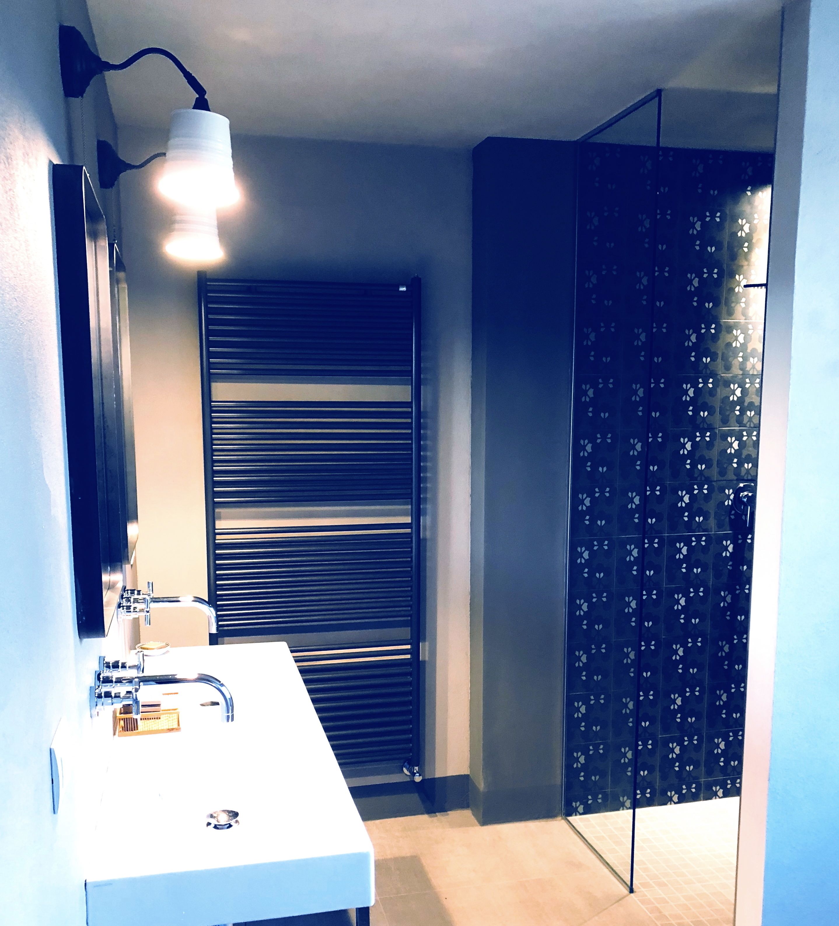 A bathroom with a white sink, a mirror, a towel rack, and a shower with a dark patterned door.