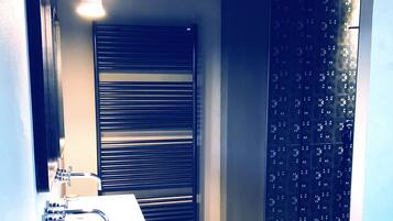A bathroom with a white sink, a mirror, a towel rack, and a shower with a dark patterned door.