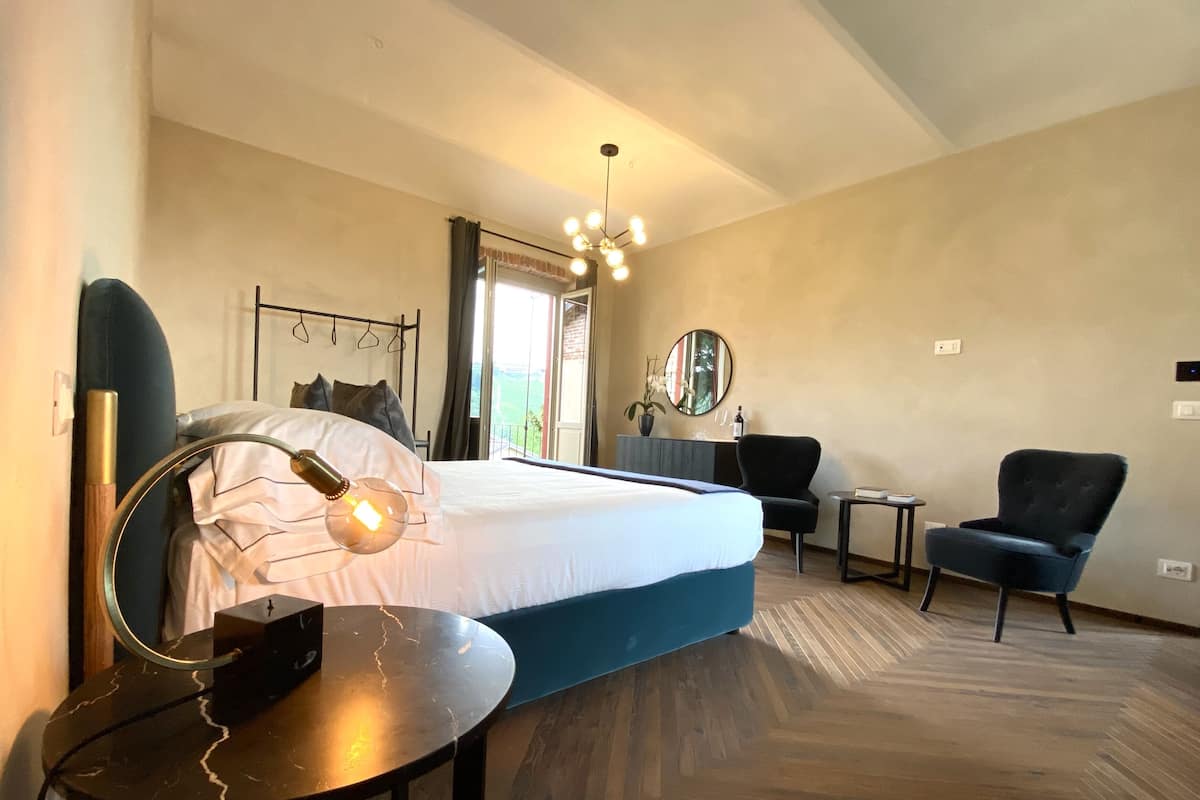 A modern hotel room with a large bed, a desk, a chair, and a small table.