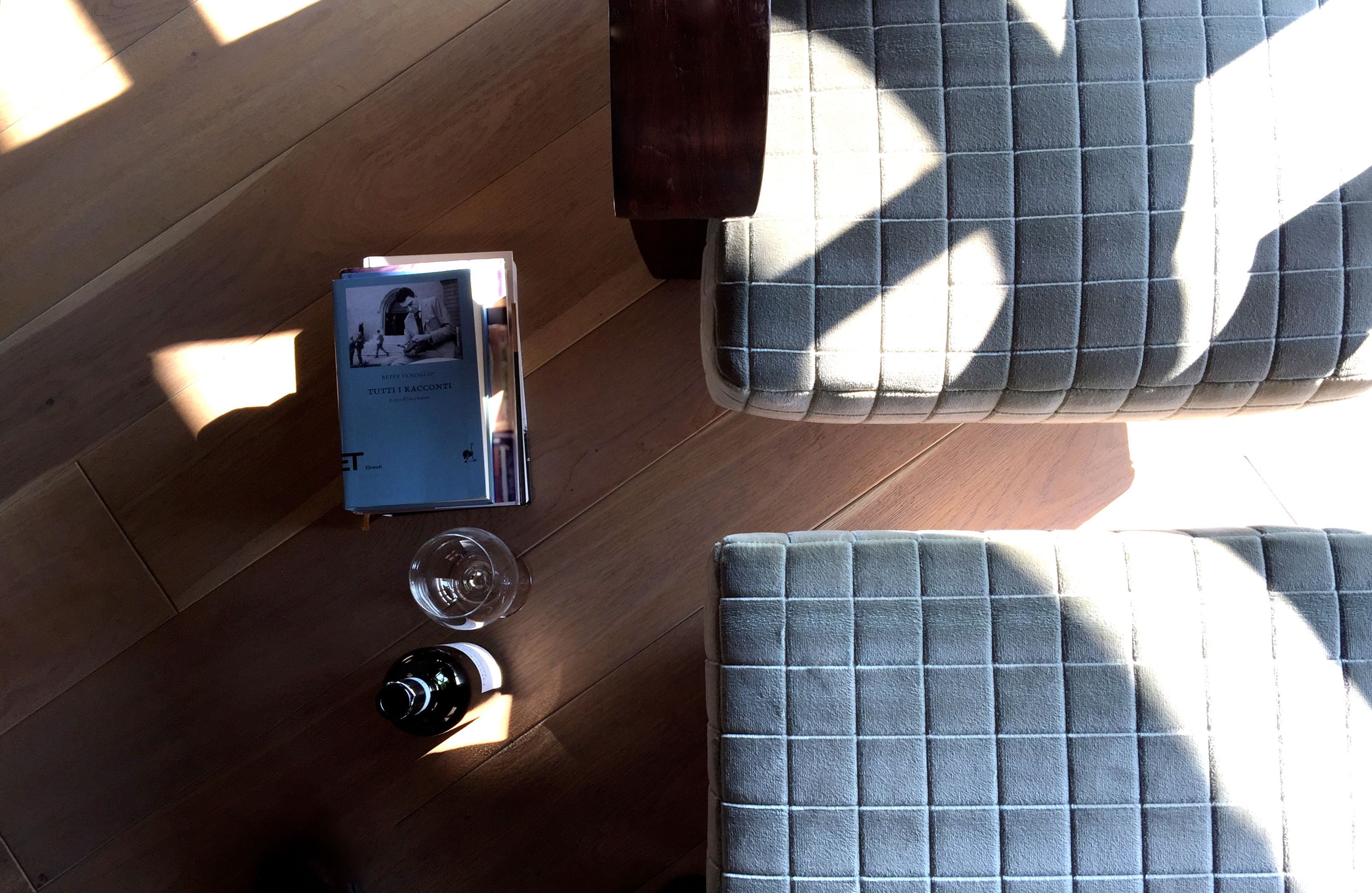 Une pièce avec un plancher en bois, un canapé gris recouvert de tissu, une petite table sur laquelle se trouvent un livre et un verre, et une table d’appoint en bois foncé.