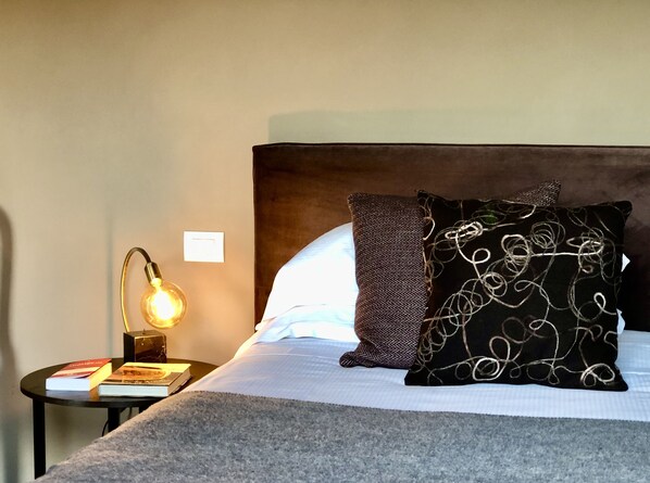 Una cama bien hecha con un cabecero oscuro, una lámpara en una mesita de noche y un par de libros.