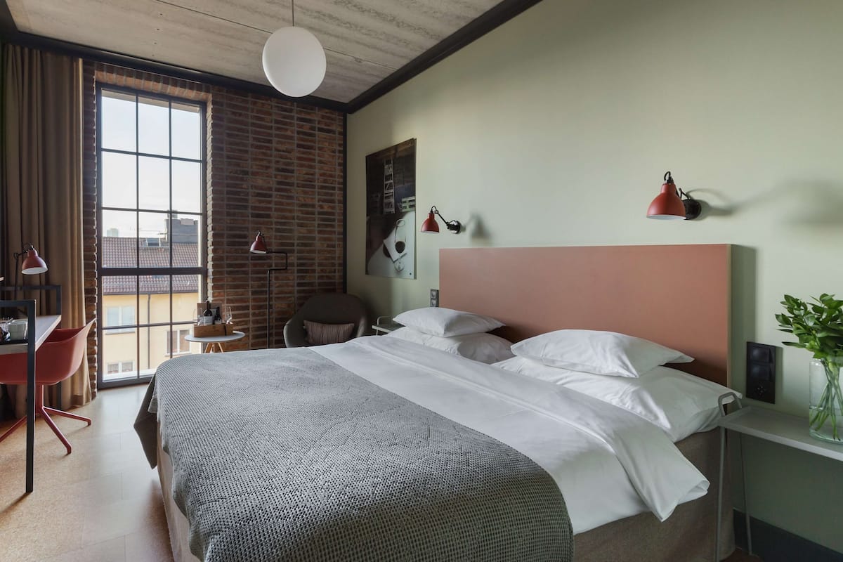 Ein modernes Hotelzimmer mit einem großen Bett, einem Schreibtisch, einem Stuhl, einem Fenster mit Vorhängen und einer Ziegelwand.