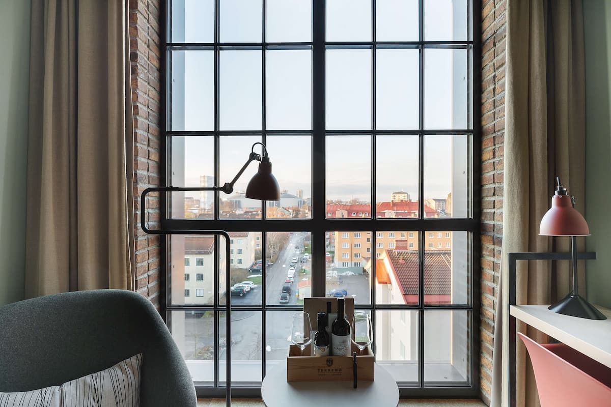 Ein Zimmer mit einem großen Fenster, einem Schreibtisch, einem Stuhl und einer Weinflasche auf der Fensterbank.
