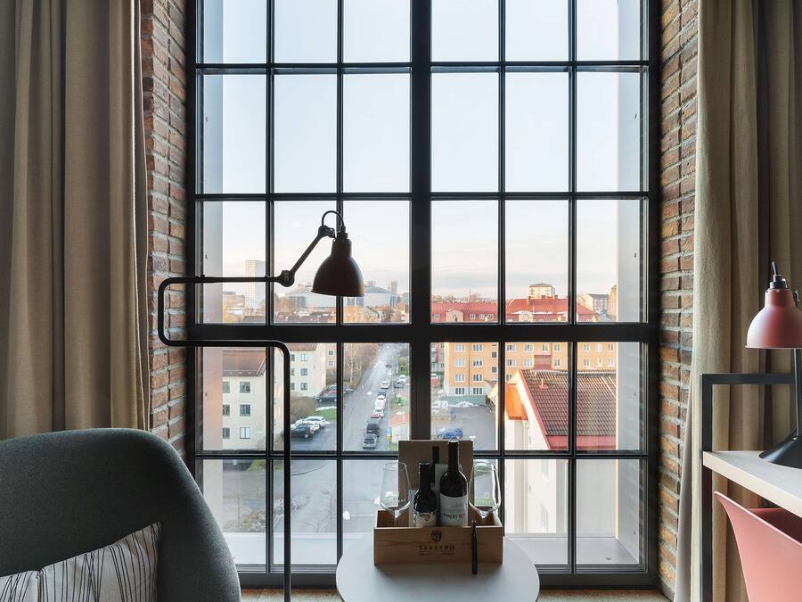 Ein Zimmer mit einem großen Fenster, einem Schreibtisch, einem Stuhl und einer Weinflasche auf der Fensterbank.
