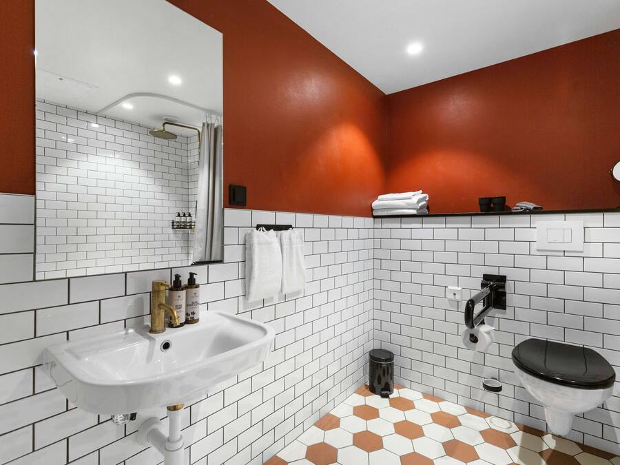 A bathroom with white and brown hexagonal tiles, a white sink with gold fixtures, a black toilet, and a mirror above the sink.