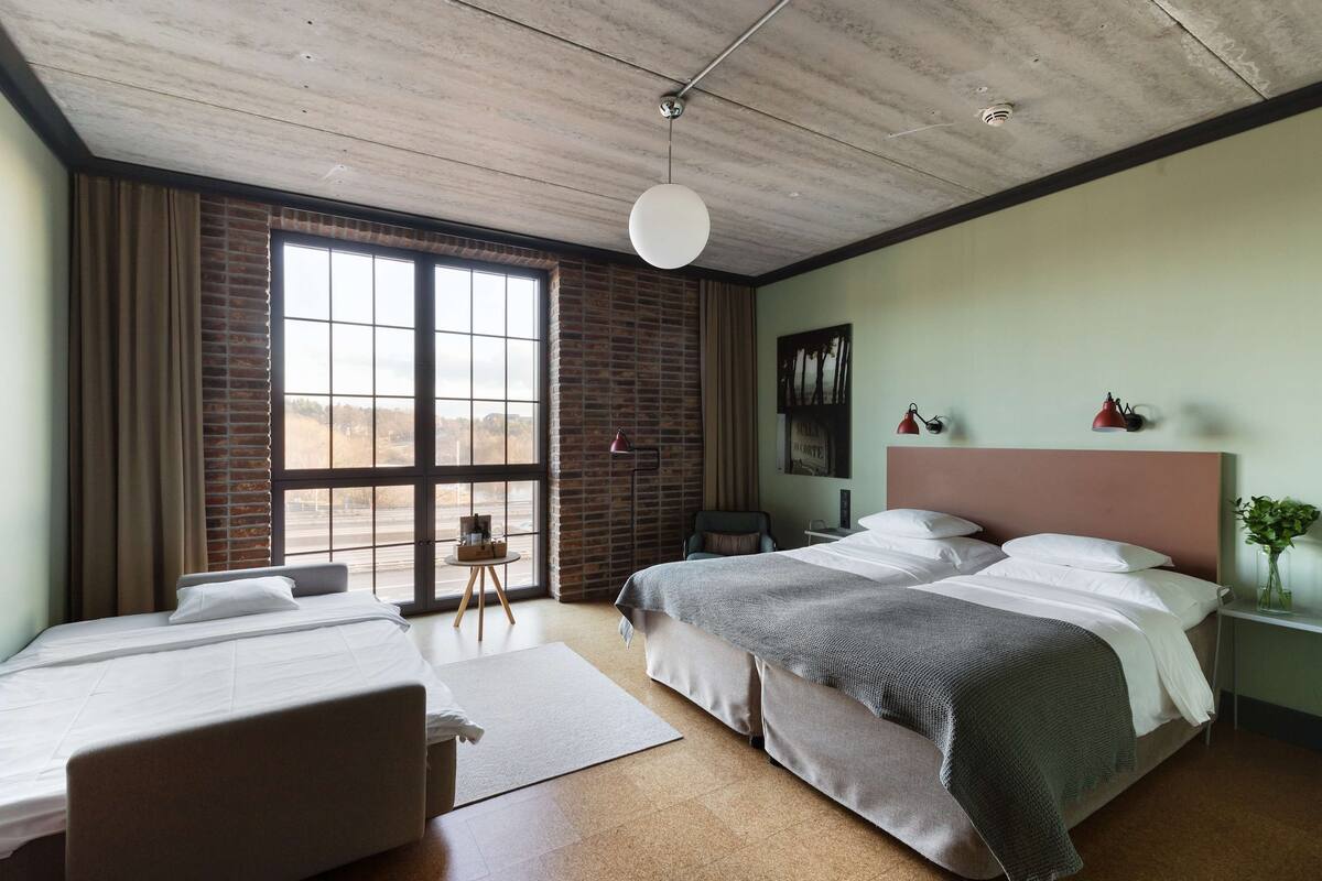 Ein Hotelzimmer mit großem Fenster, einem Bett, einem Schreibtisch und einem Stuhl.