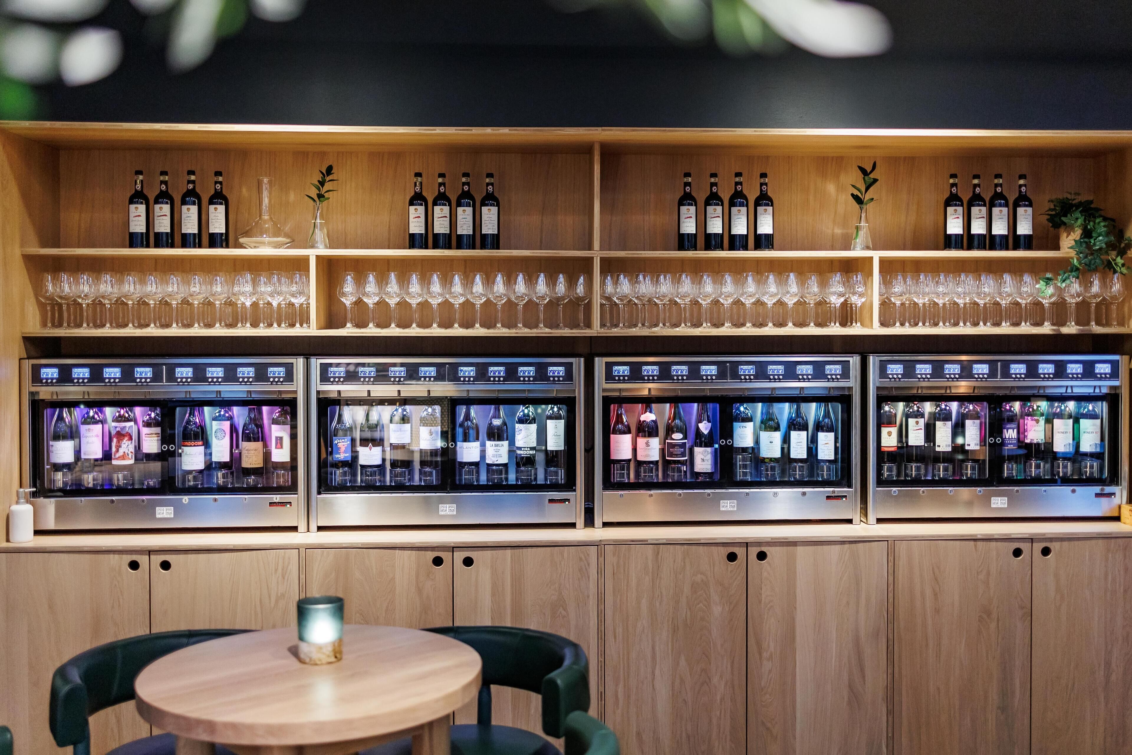 En bardisk med hyllor fulla av vinflaskor och glas, samt ett kylskåp där vinflaskor visas upp.