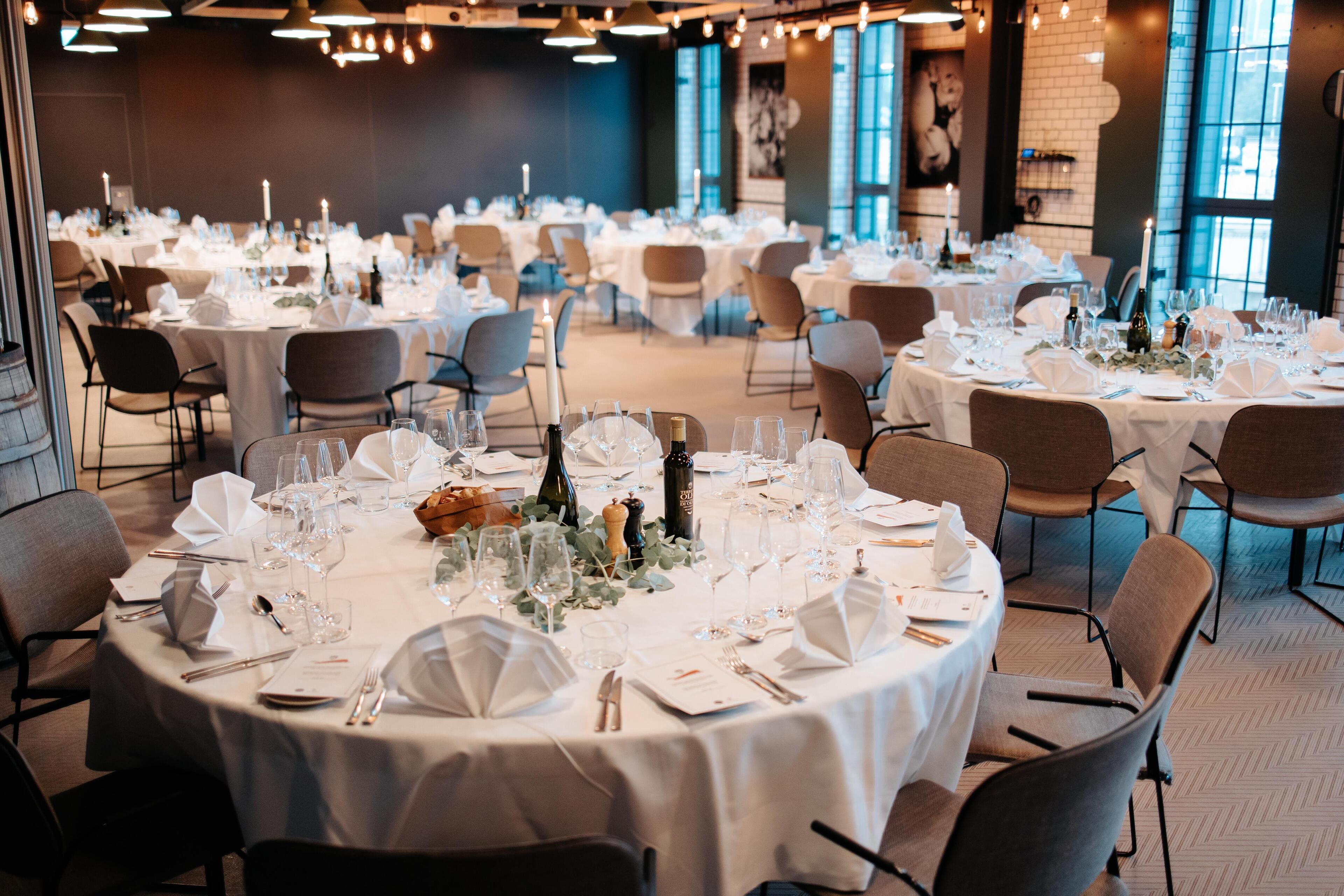 A banquet hall with round tables set for a formal event, featuring white tablecloths, glassware, and candles.