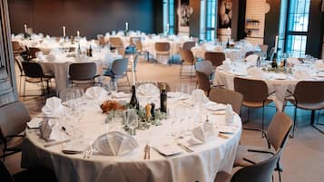 Una sala de banquetes amb taules rodones preparades per a un esdeveniment formal, amb tovallons blancs, vetrereria i espelmes.