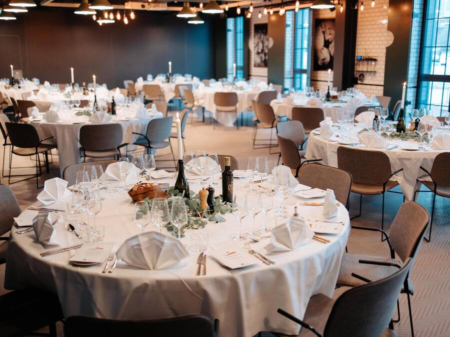 A banquet hall with round tables set for a formal event, featuring white tablecloths, glassware, and candles.