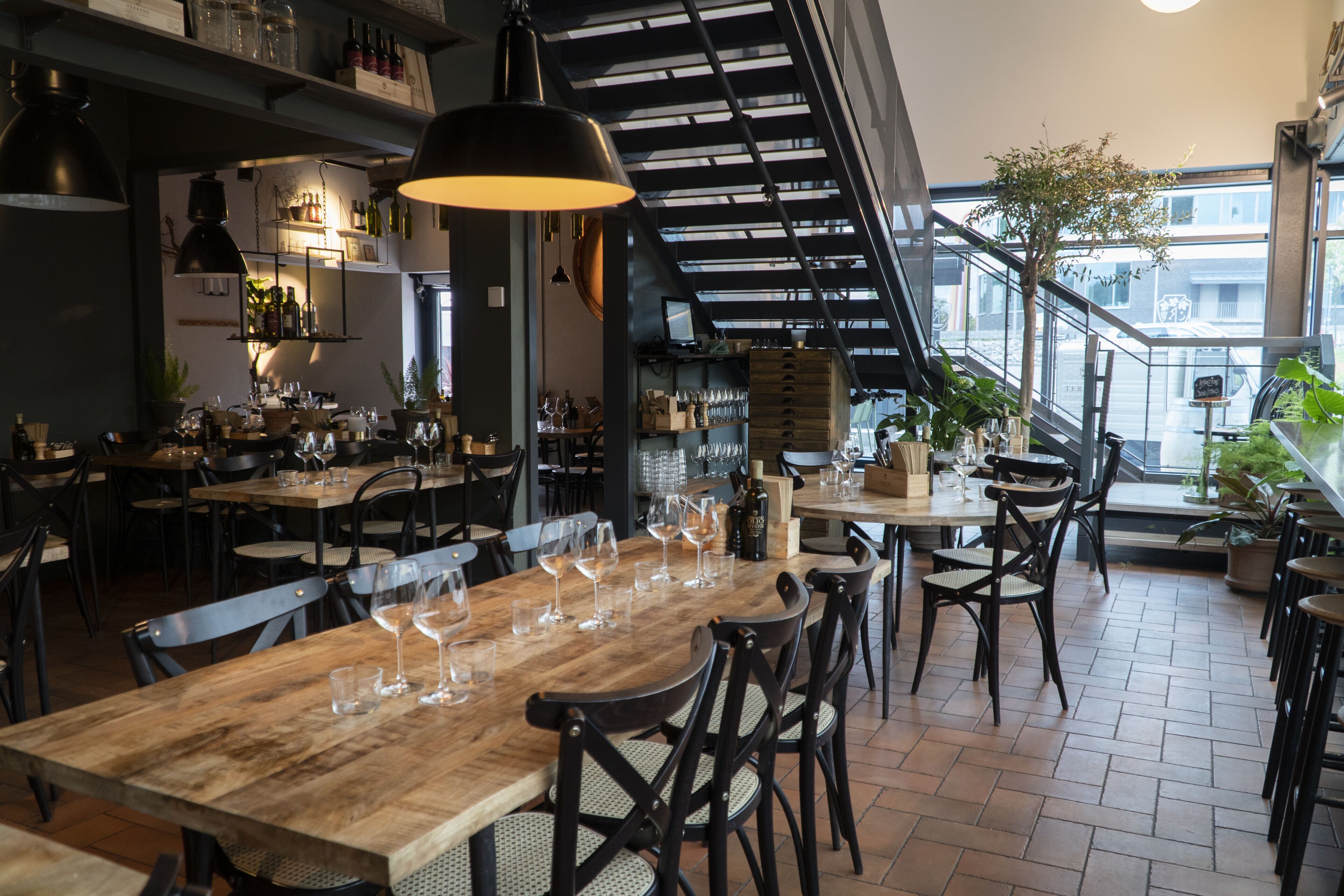 L’intérieur d’un restaurant, avec des tables en bois, des chaises noires et des lampes suspendues.