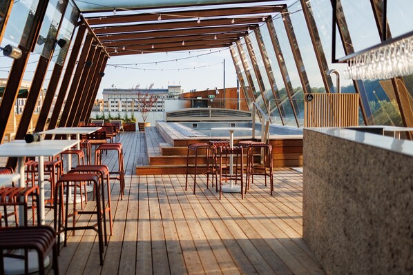 Une terrasse avec des tables et des chaises, un jacuzzi et une vue sur la ville.