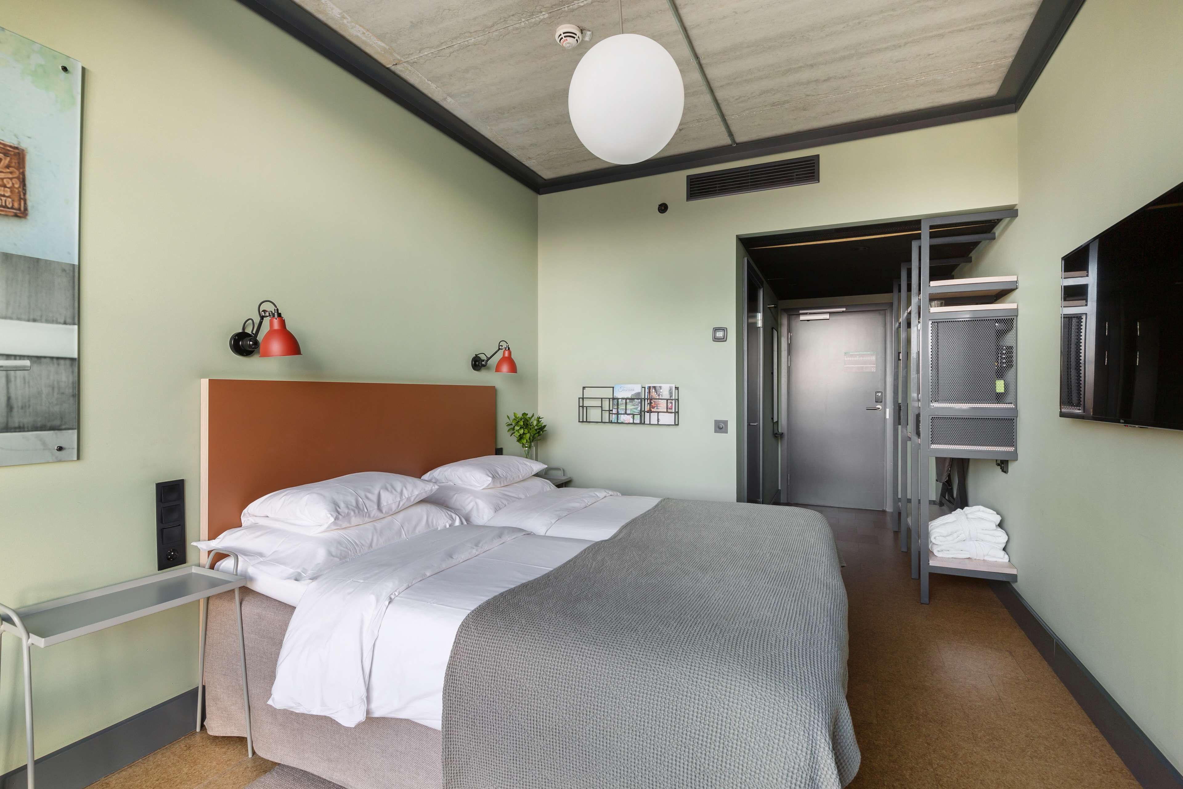 Una camera d'albergo con un letto, una scrivania, una lampada rossa e un armadio.
