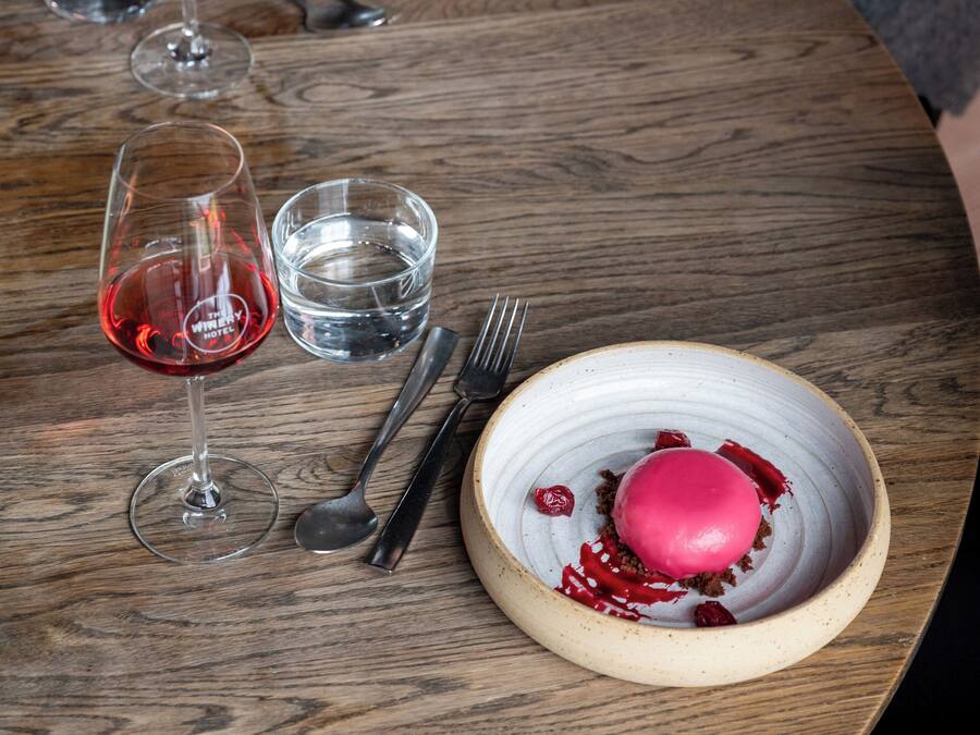 A wooden table with a dessert, wine glasses, and cutlery.