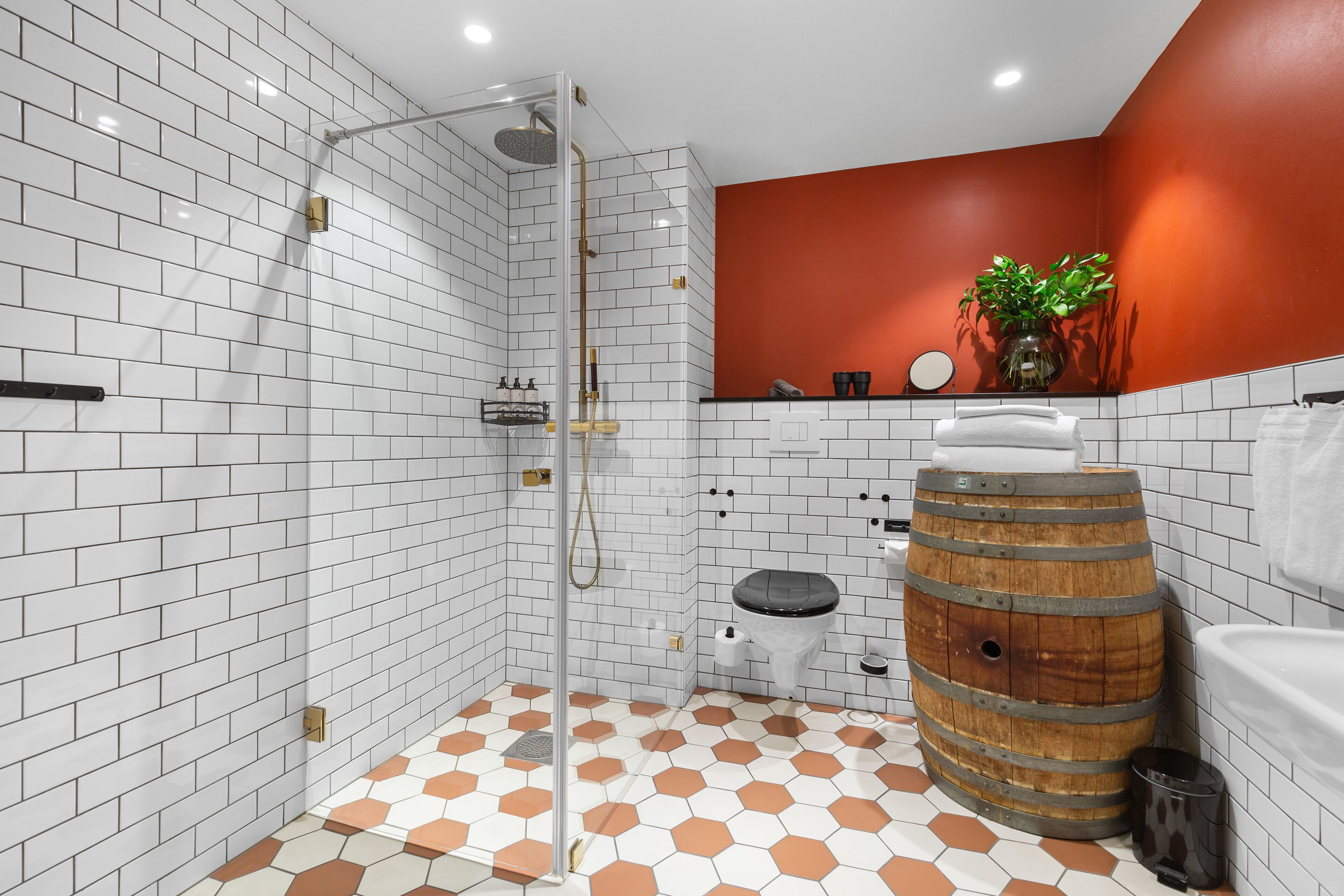 Een badkamer met witte metro betegeling, een vloer met een honingraatpatroon, een houten vat, een toilet en een douchegedeelte.