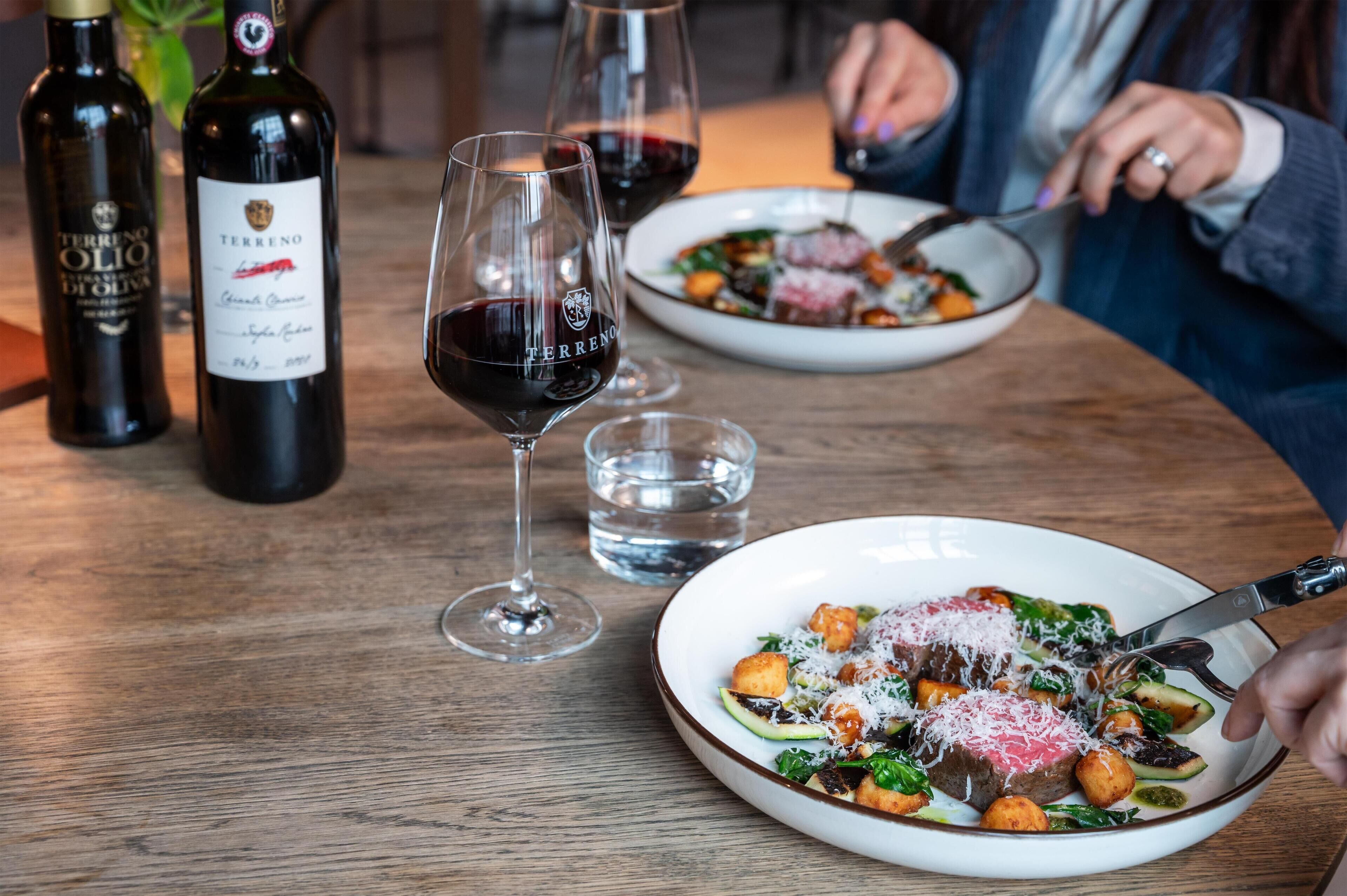 A dining table with wine bottles, glasses, and a plate of food.