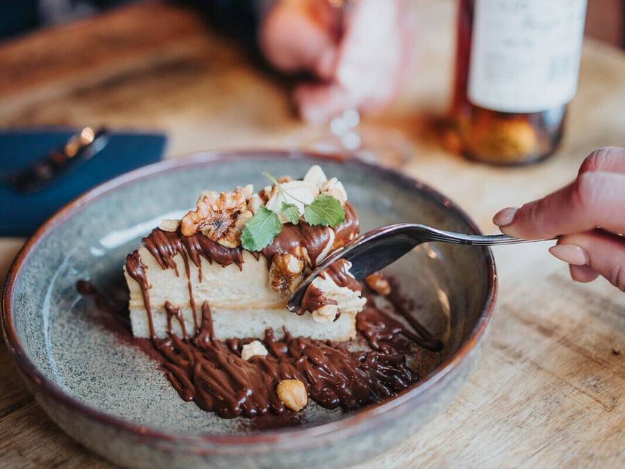 Un dessert aux noix, nappé de sauce au chocolat, présenté sur une assiette, avec un verre à vin et une bouteille de vin sur la table.