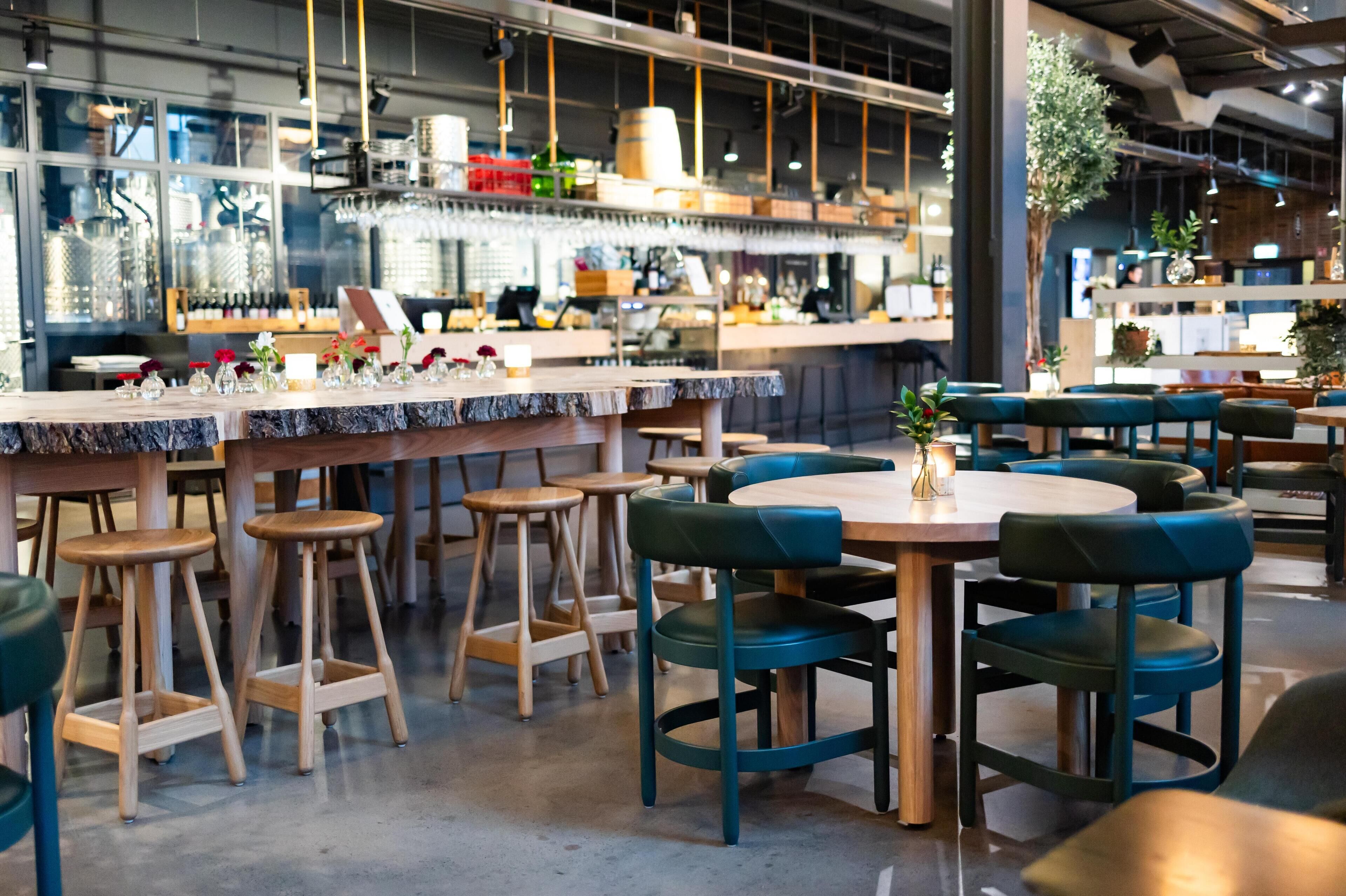 Un interior de restaurante moderno con asientos de madera y tapizados, una zona de bar y equipo de cocina a la vista.